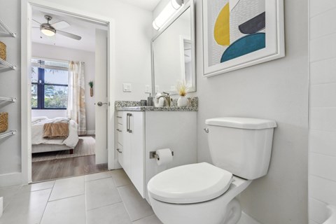 A white toilet in a bathroom with a mirror and a painting on the wall.