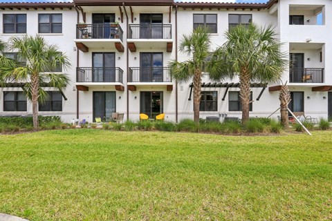 A white apartment building with balconies and palm trees in front.