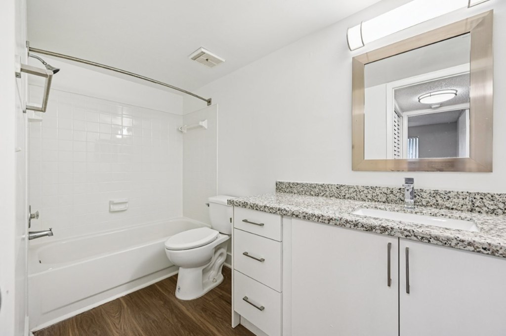 A white bathroom with a marble counter top and a large mirror.