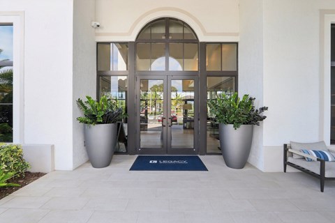 A building entrance with a blue mat and two large pots of plants.