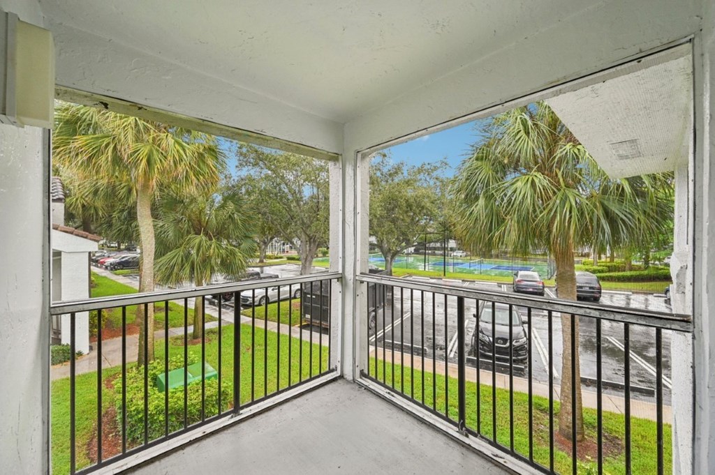 A balcony with a metal railing and a view of a street with cars and palm trees.