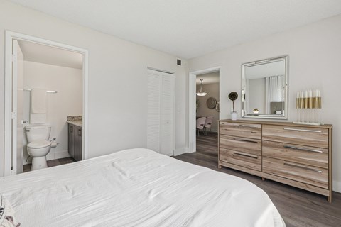 A white bed in a room with a wooden dresser and mirror.