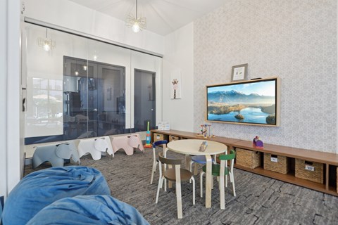 A room with a table, chairs, and a television displaying a landscape.