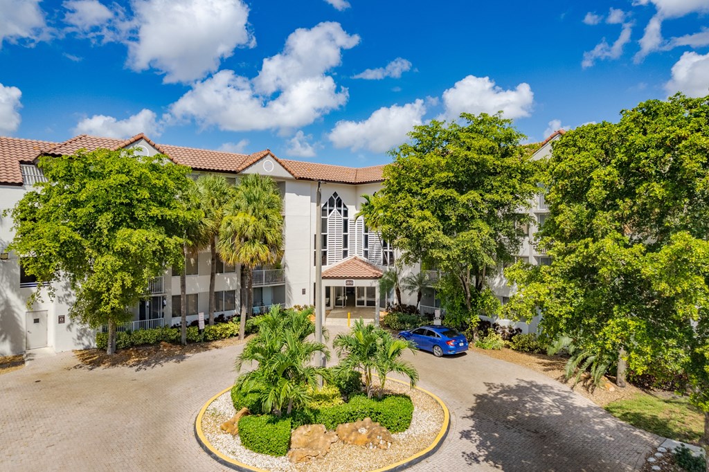an apartment building with palm trees and a blue car parked in front