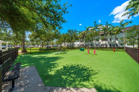 A green artificial turf field with a bench and trees in the background.