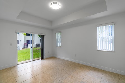 A spacious room with tiled flooring and a sliding glass door leading to a backyard.