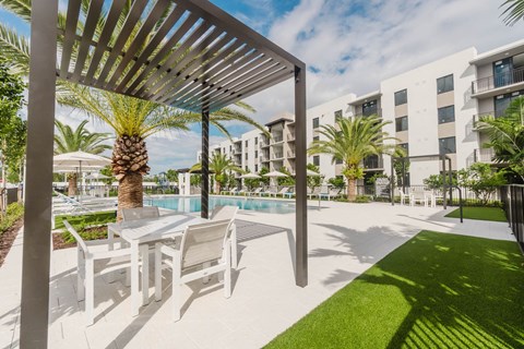 A patio with white chairs and a table under a pergola.