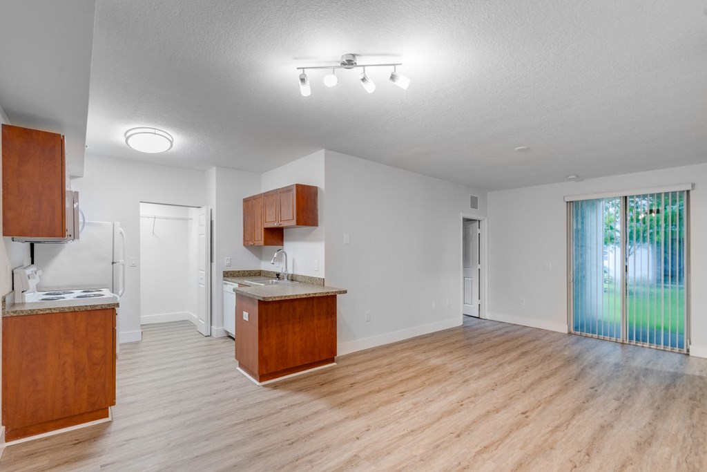 an empty living room and kitchen with wooden floors and a sliding glass door