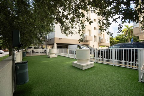 A white fence surrounds a green artificial turf area with a white pillar in the middle.