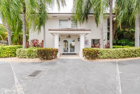 A white building with a black door and windows surrounded by greenery.