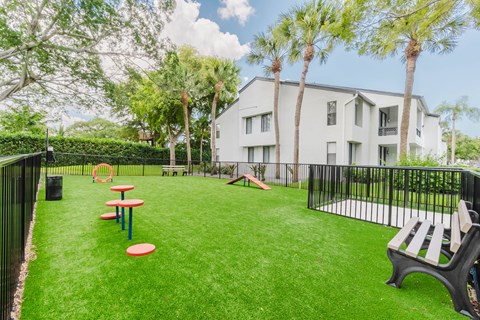 A playground area with a slide, picnic tables, and a bench in front of a white building.