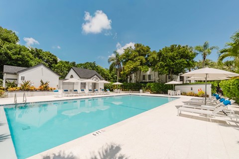 A large swimming pool surrounded by lounge chairs and umbrellas with a house in the background.