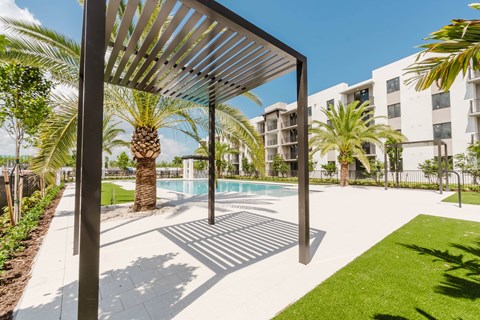 A pool area with a sunshade structure and palm trees.