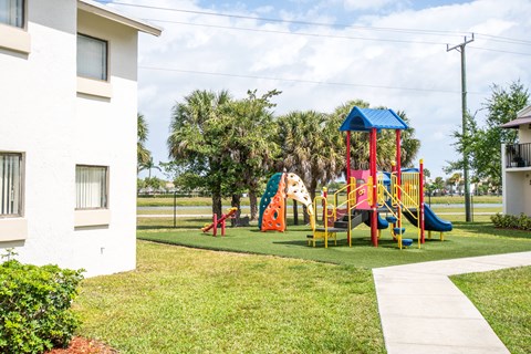 A playground with a blue roof and a slide is in front of a white building.