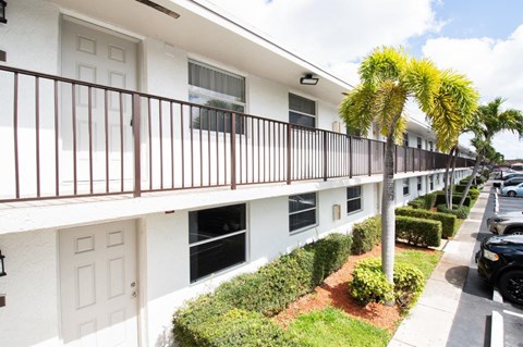 A row of white apartment buildings with brown railings and a tree in front.