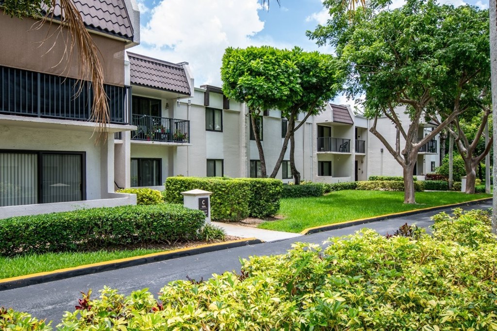 A row of white apartment buildings with green trees in front.
