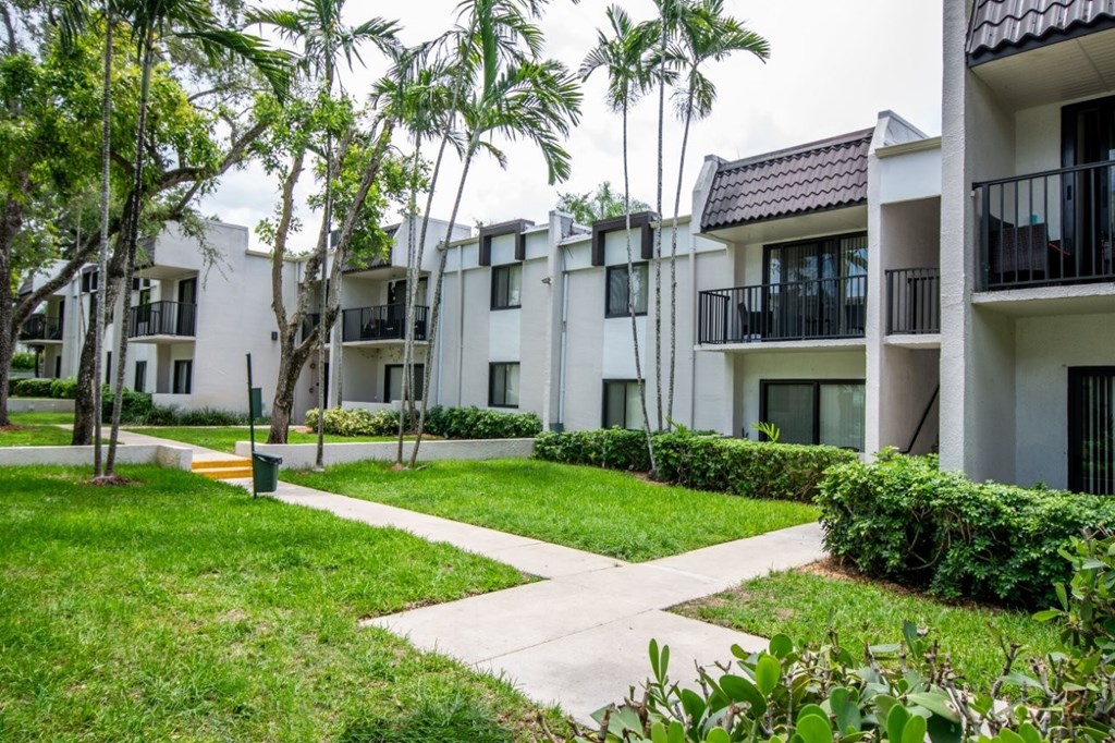 A row of white apartment buildings with balconies and greenery in front.