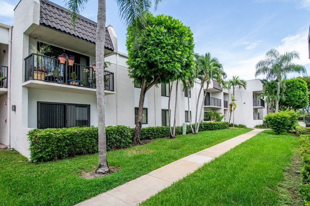 A row of white apartment buildings with green trees in front.