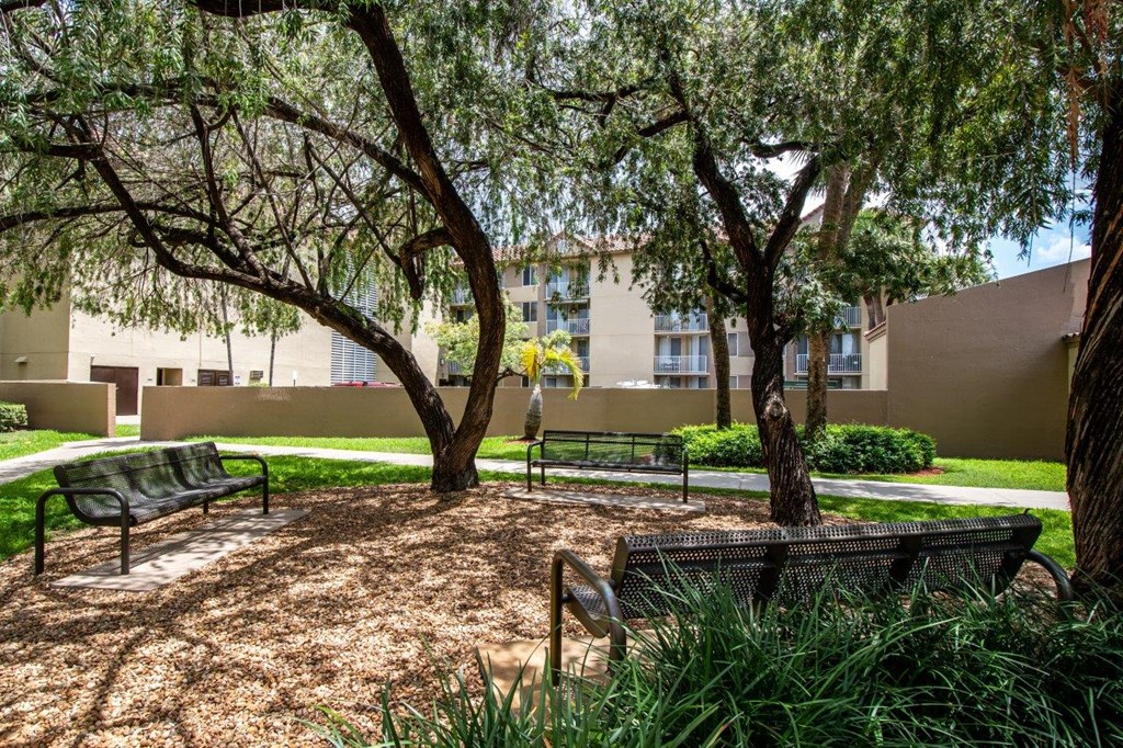 a park with benches and trees in front of an apartment building