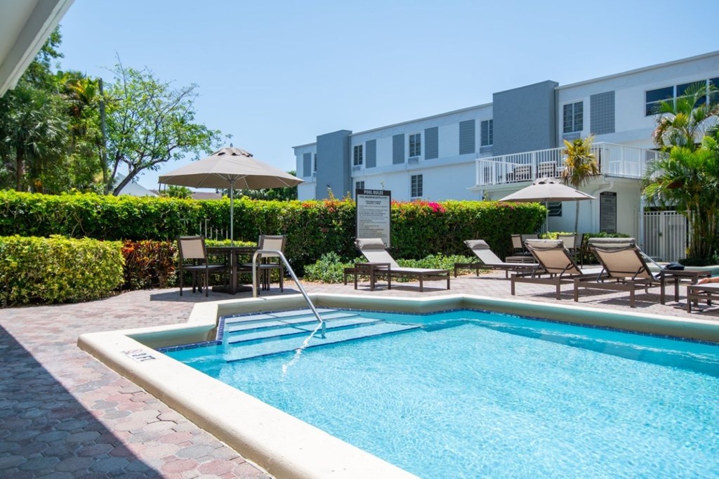 A pool surrounded by chairs and a building in the background.