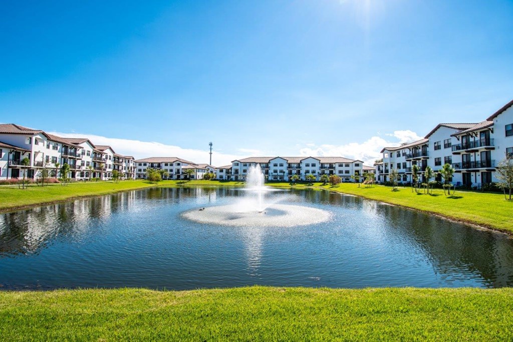 a fountain in the middle of a pond with apartments in the background