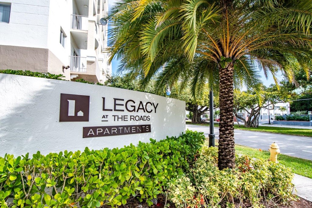 a sign for legacy at the rocks apartments in front of a palm tree