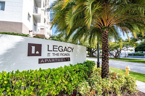 a sign for legacy at the rocks apartments in front of a palm tree