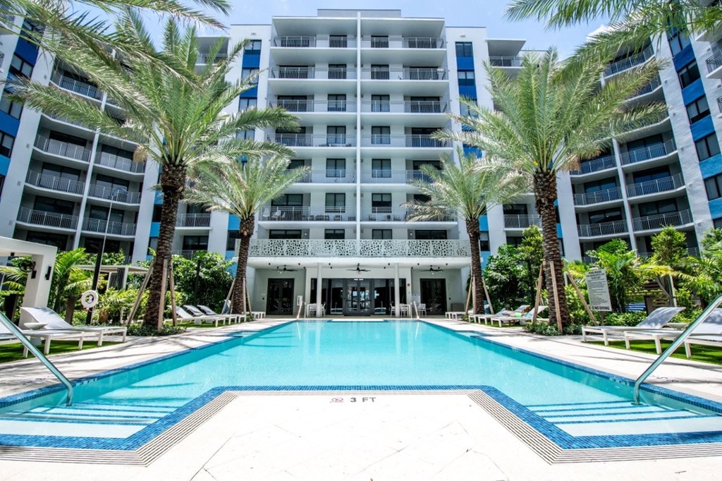 a large swimming pool in front of an apartment building with palm trees