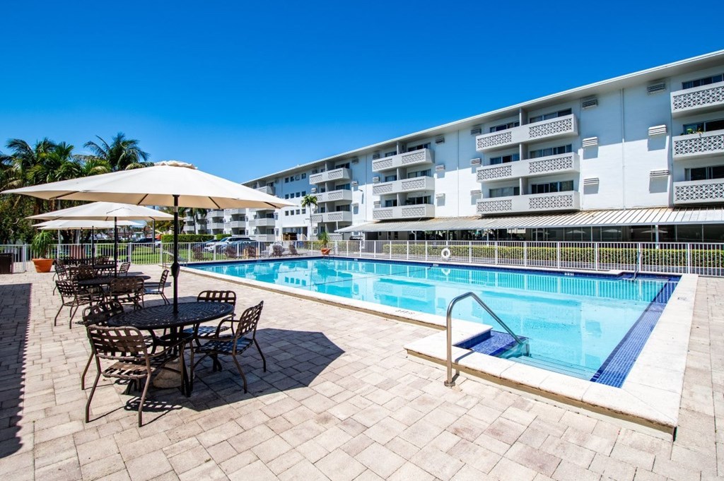 A pool area with a table and chairs and umbrellas.