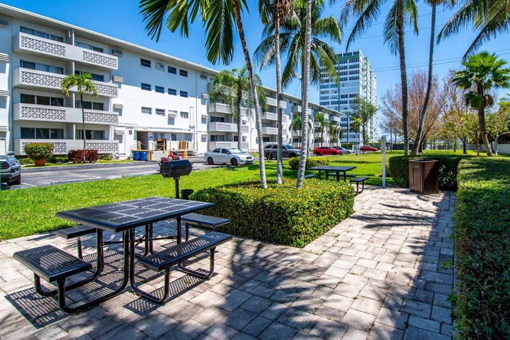 A picnic table is surrounded by palm trees and apartment buildings.