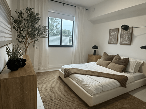 A bedroom with a large bed and a tree in a vase on a wooden dresser.