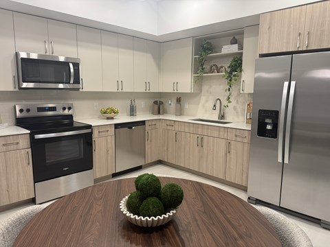 A modern kitchen with a wooden table and a bowl of green vegetables on it.
