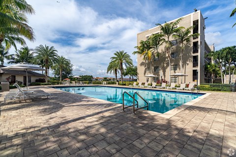 A swimming pool surrounded by palm trees and a building in the background.