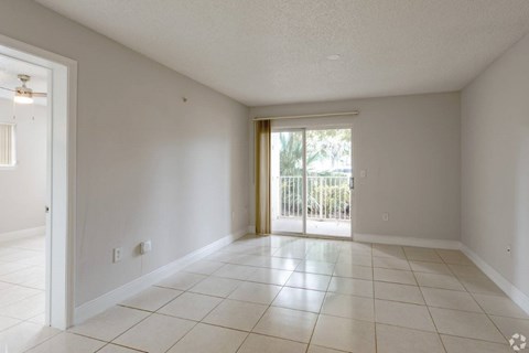 A spacious room with white tiled flooring and a sliding glass door leading to a balcony.