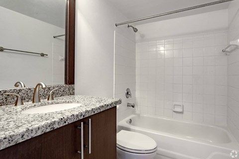 A white tiled bathroom with a marble countertop and a white toilet.