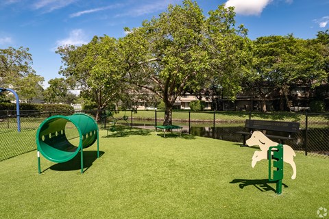 A dog slide and a dog-shaped bench are in a dog park.