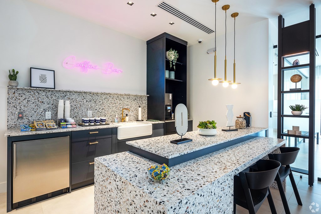 A modern kitchen with a granite countertop and a neon sign that says "Coffee Bar".