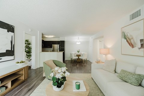 A living room with a white couch, a coffee table with a vase of flowers, and a painting on the wall.
