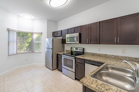 A kitchen with a refrigerator, oven, microwave, sink, and cabinets.