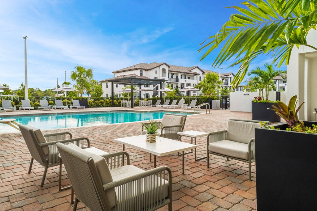 a swimming pool with chairs and tables and a building in the background