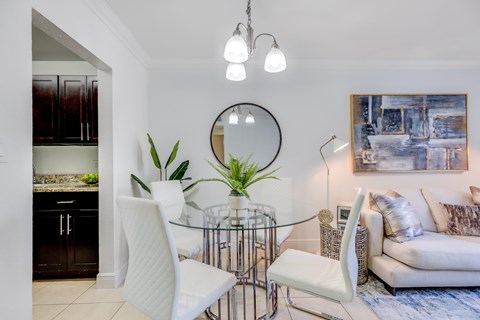 A modern dining room with a glass table and white chairs.