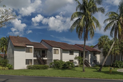 A white building with a red roof and palm trees in front.
