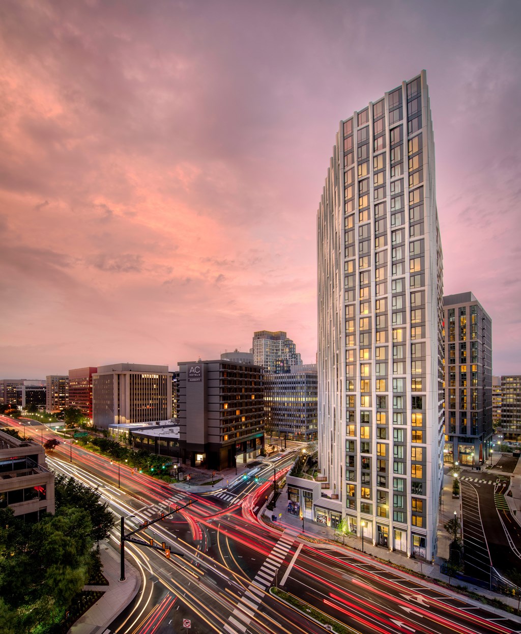 A tall building with many windows is lit up at dusk.
