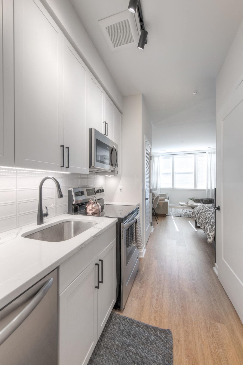 Galley kitchen with cupboards, sink, dishwasher, microwave, white cabinets, and a sink