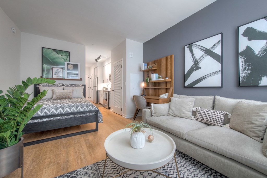 Studio living room space with couch, coffee table, bed, workspace, and kitchen