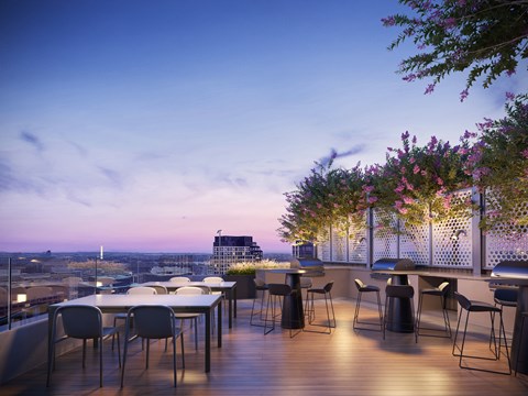 A balcony with a table and chairs overlooking a cityscape at dusk.