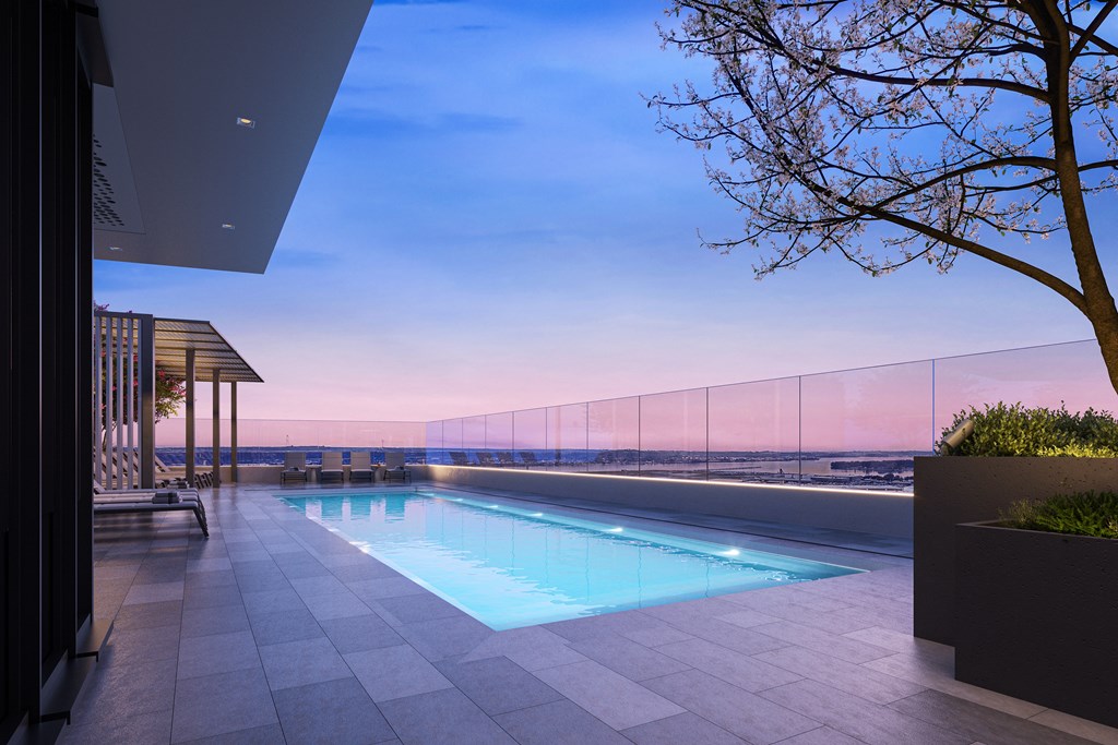 A modern outdoor pool area with a tree and a fence in the background.
