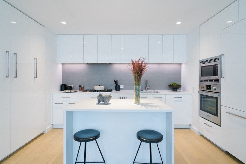 a kitchen with white cabinets and a white island with two black stools