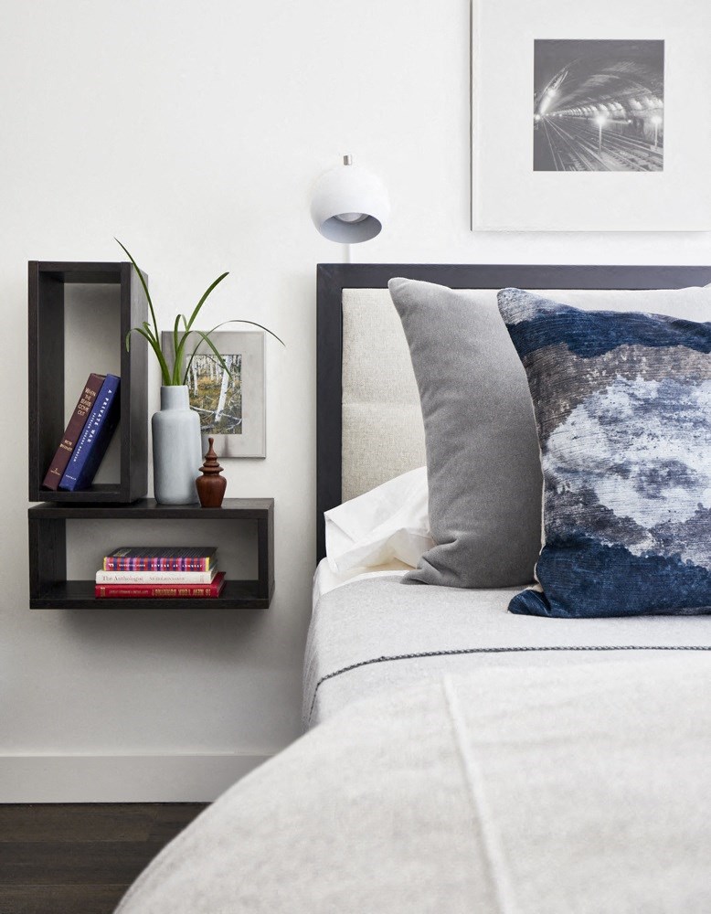 a bed with a blue and white pillow and a shelf with books and a plant