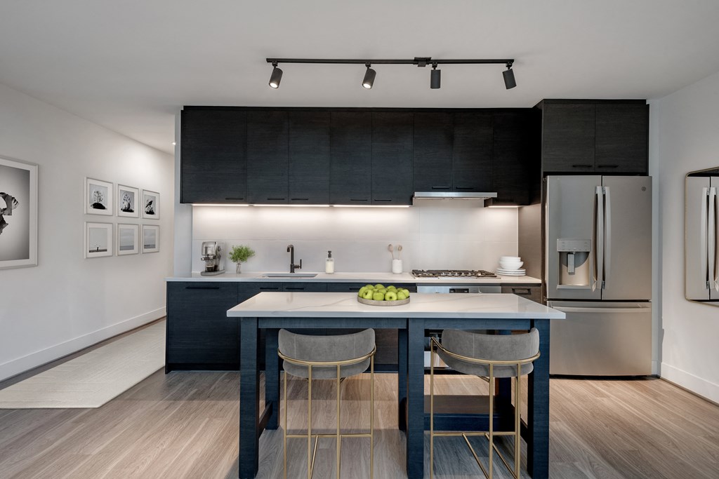 a kitchen with black cabinets and a blue island with three chairs